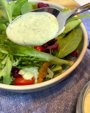 fresh green goddess dressing in spoon drizzled over salad greens