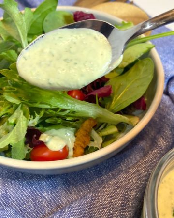 fresh green goddess dressing in spoon drizzled over salad greens