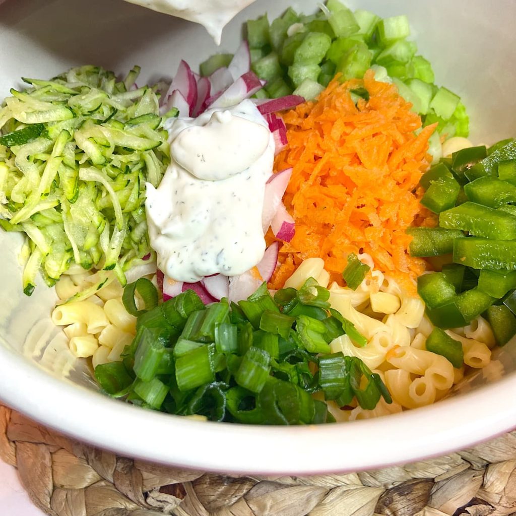 Adding dressing to vegetable pasta salad