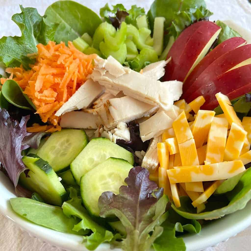 bowl of salad with greens, chopped vegetables, fruit, turkey, and cheese.