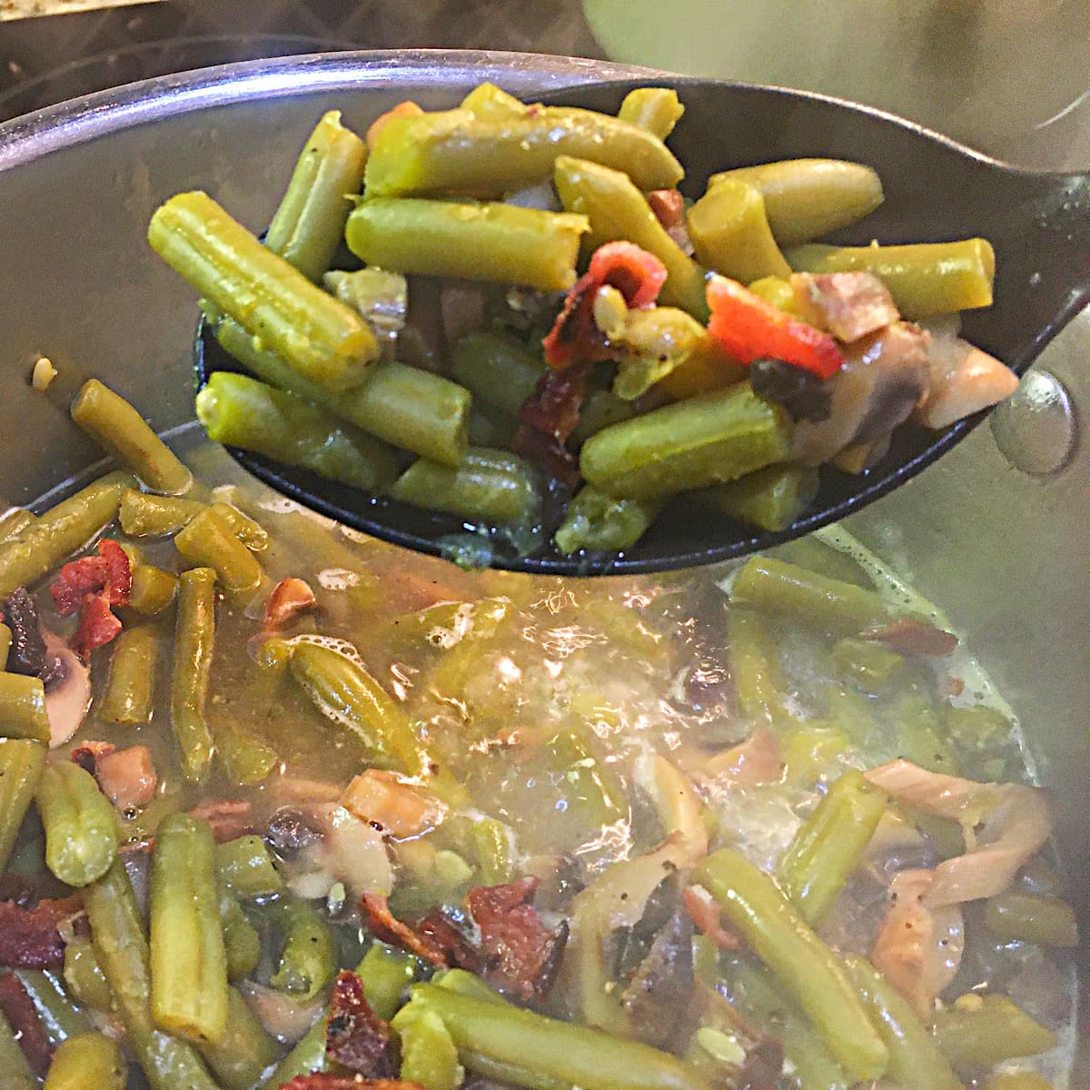 spoonful of green beans with bacon, mushrooms, and onion.