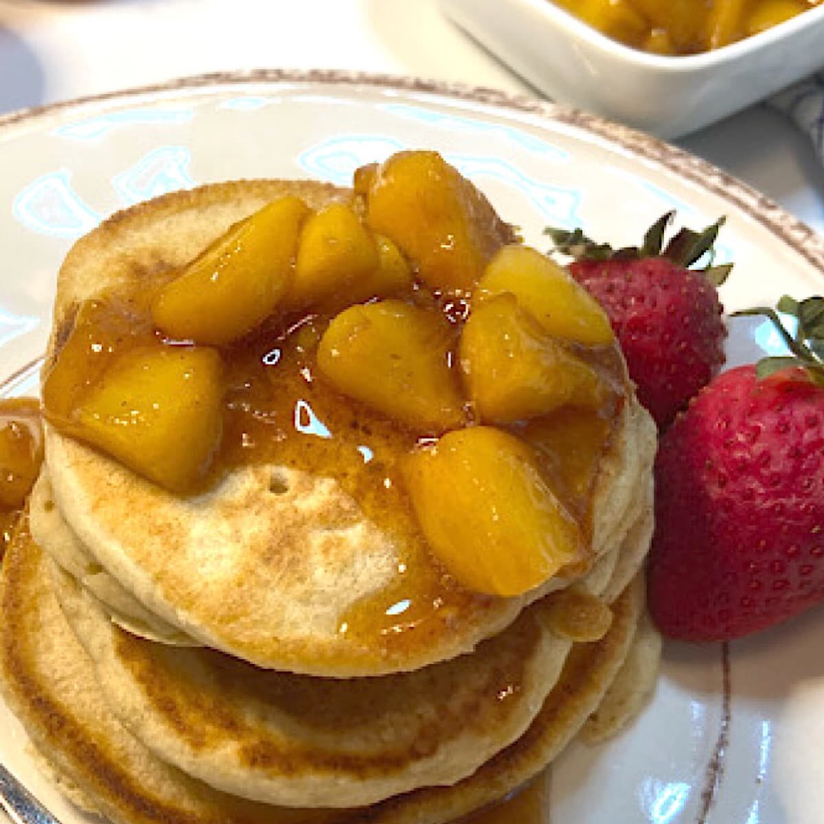 Stack of pancakes with fruit sauce and strawberries on plate.