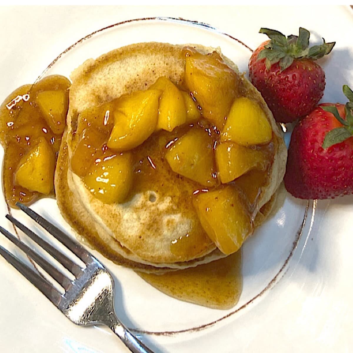 Plate of fluffy whole wheat pancakes served with cooked fruit and pur maple syrup.