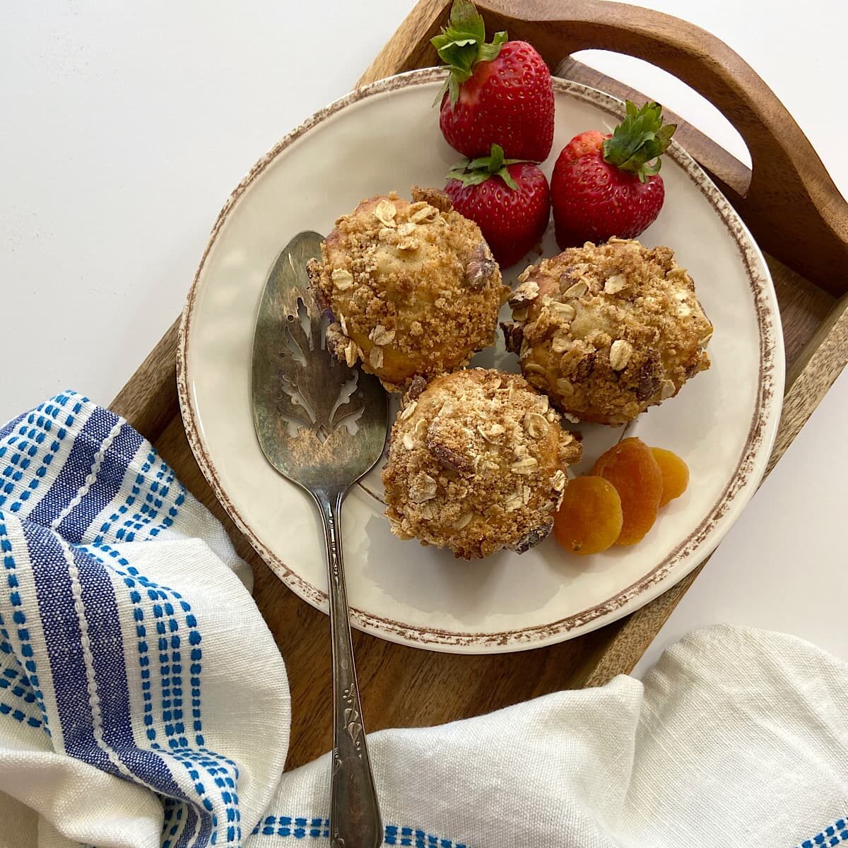 three apricot oat muffins on a plate with strawberries and dried apricots