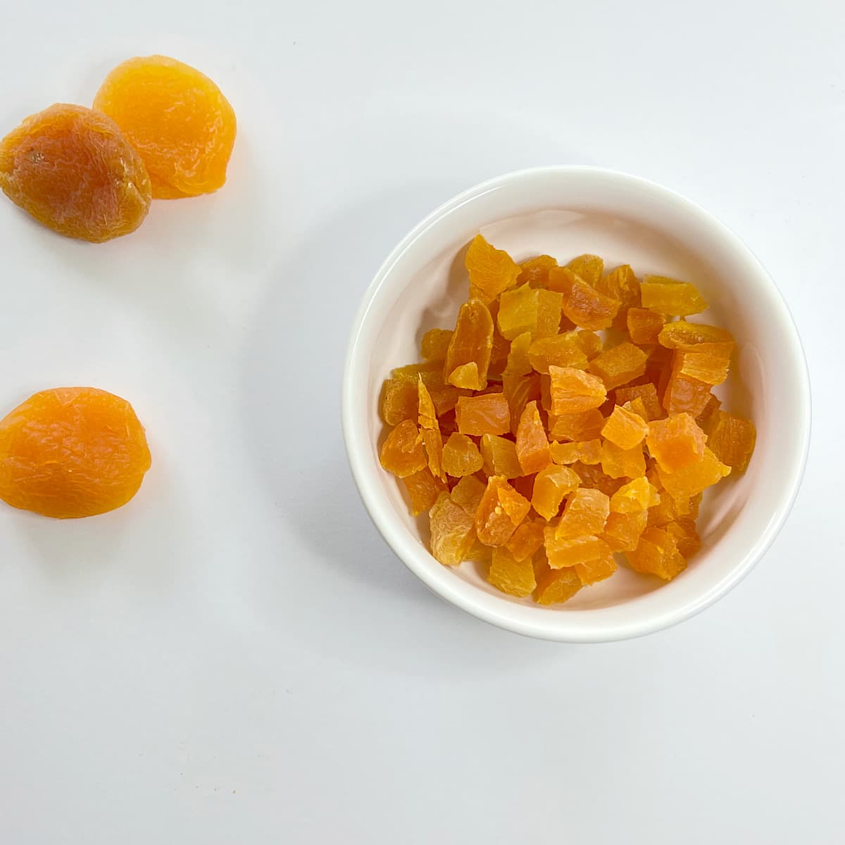 chopped dried apricots in a bowl next to 3 whole apricots