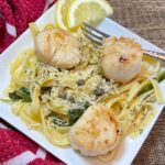 pan seared scallops with capers spinch and a lemon broth sauce on a plate.