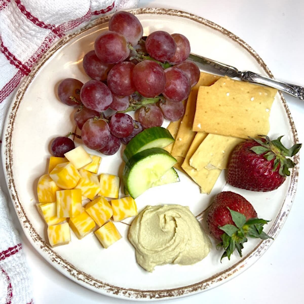 fruit, cheese, vegetables, crackers and hummus on plate.