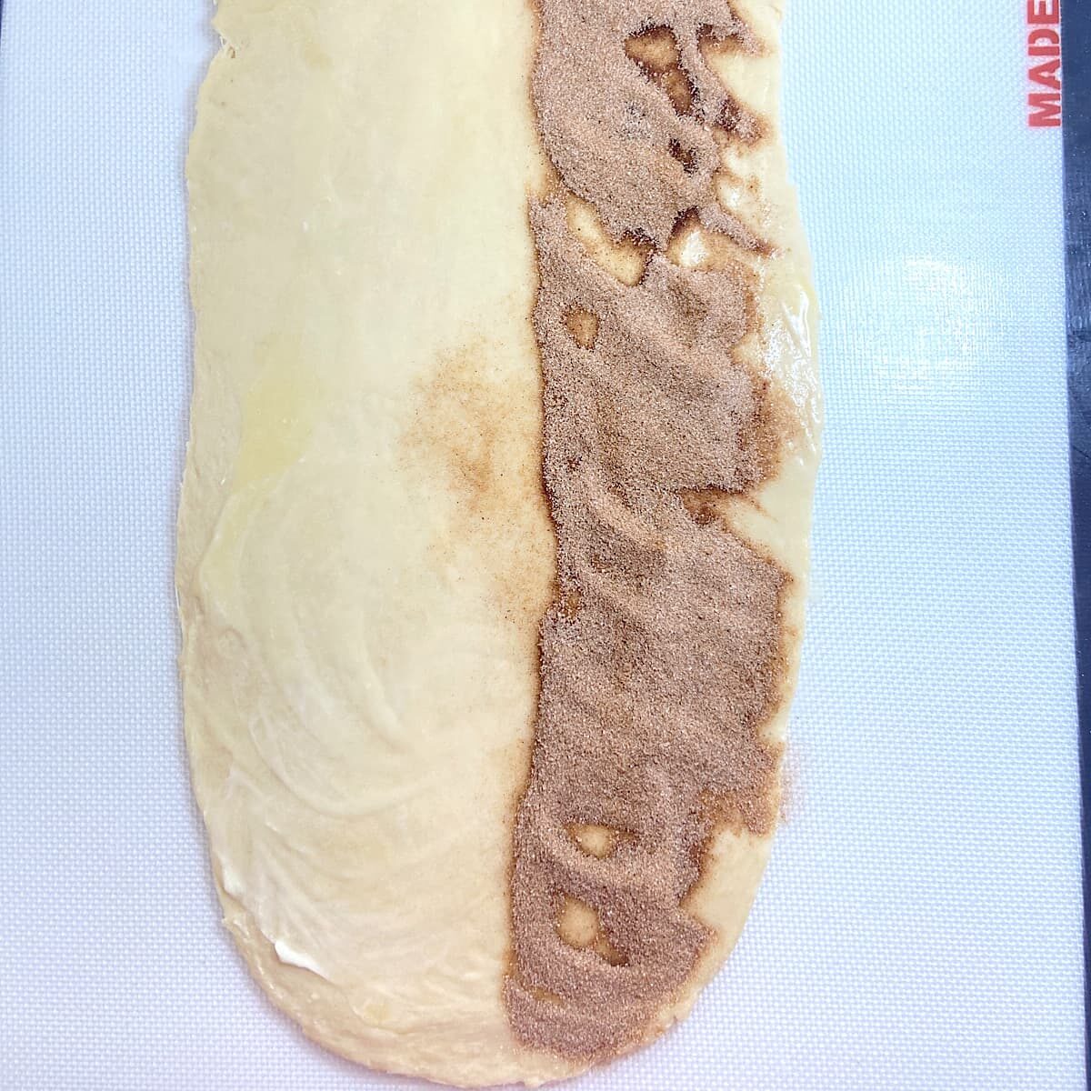 picture of rolled dough with half the length of dough sprinkled with cinnamon sugar mix.