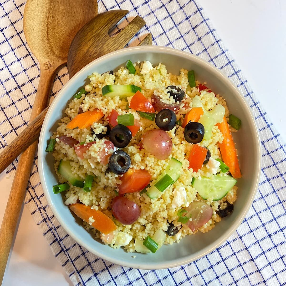 bowl of vegetable couscous salad with wooden serving spoons.