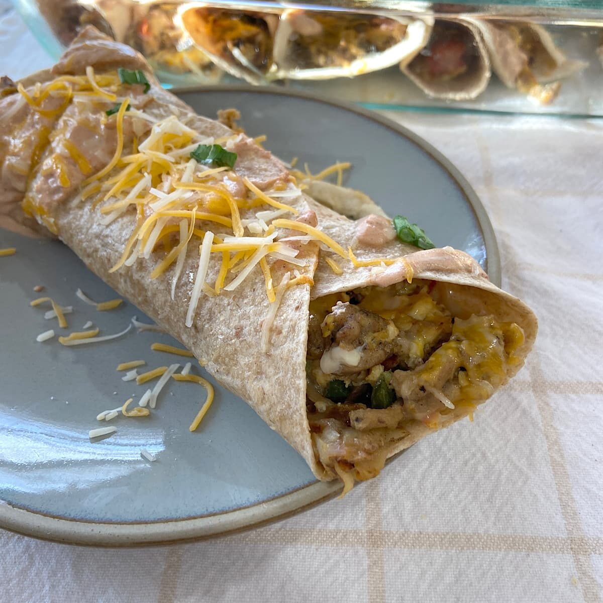 breakfast burrito on plate with pan of burritos in background.