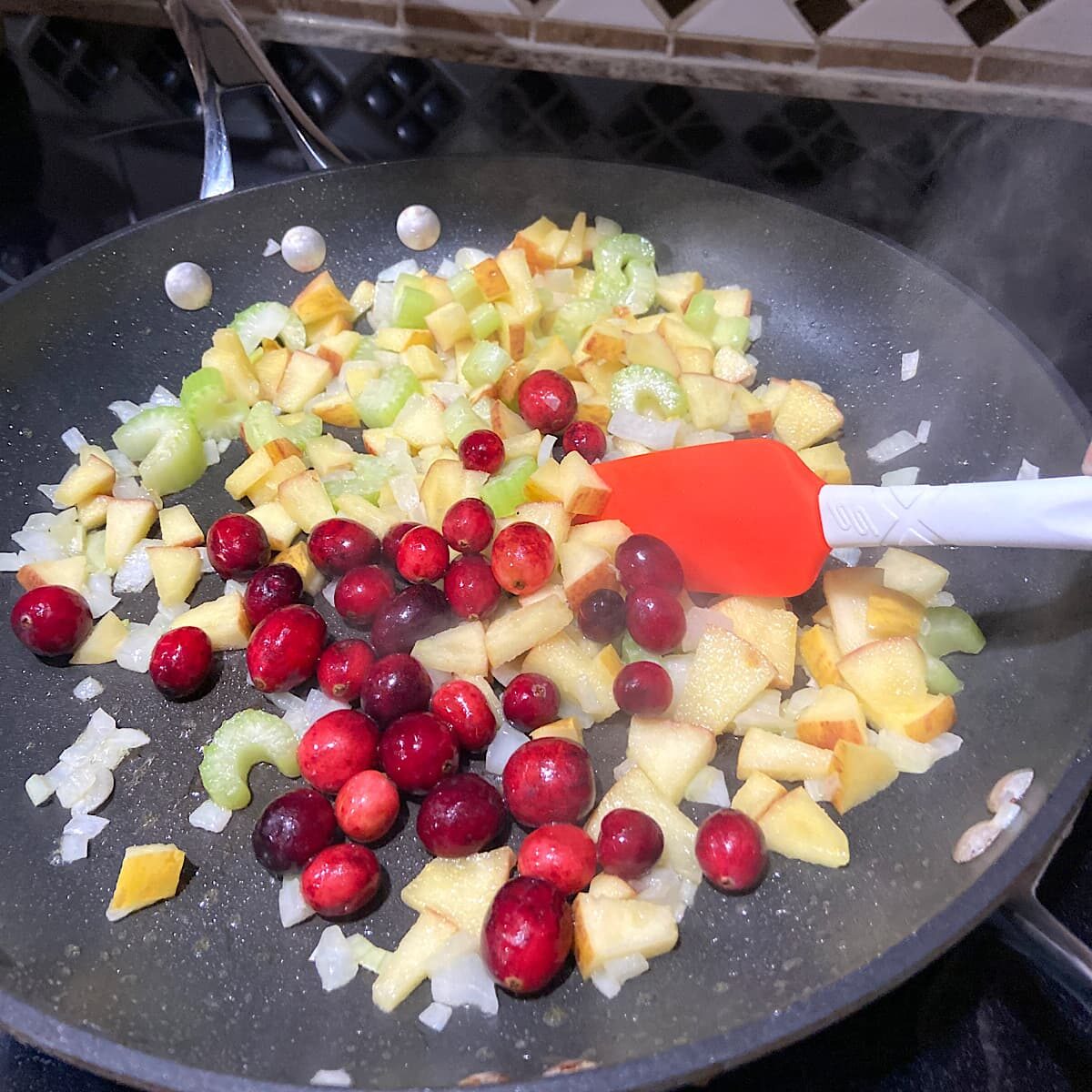 picture of heating apple, cranberry, onion and celery in pan.