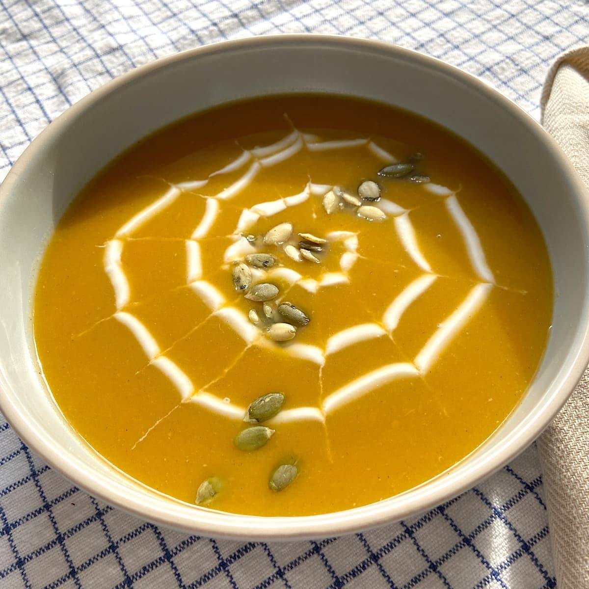 acorn squash soup in bowl with a drizzle of Greek yogurt and sprinkle of pumpkin seeds