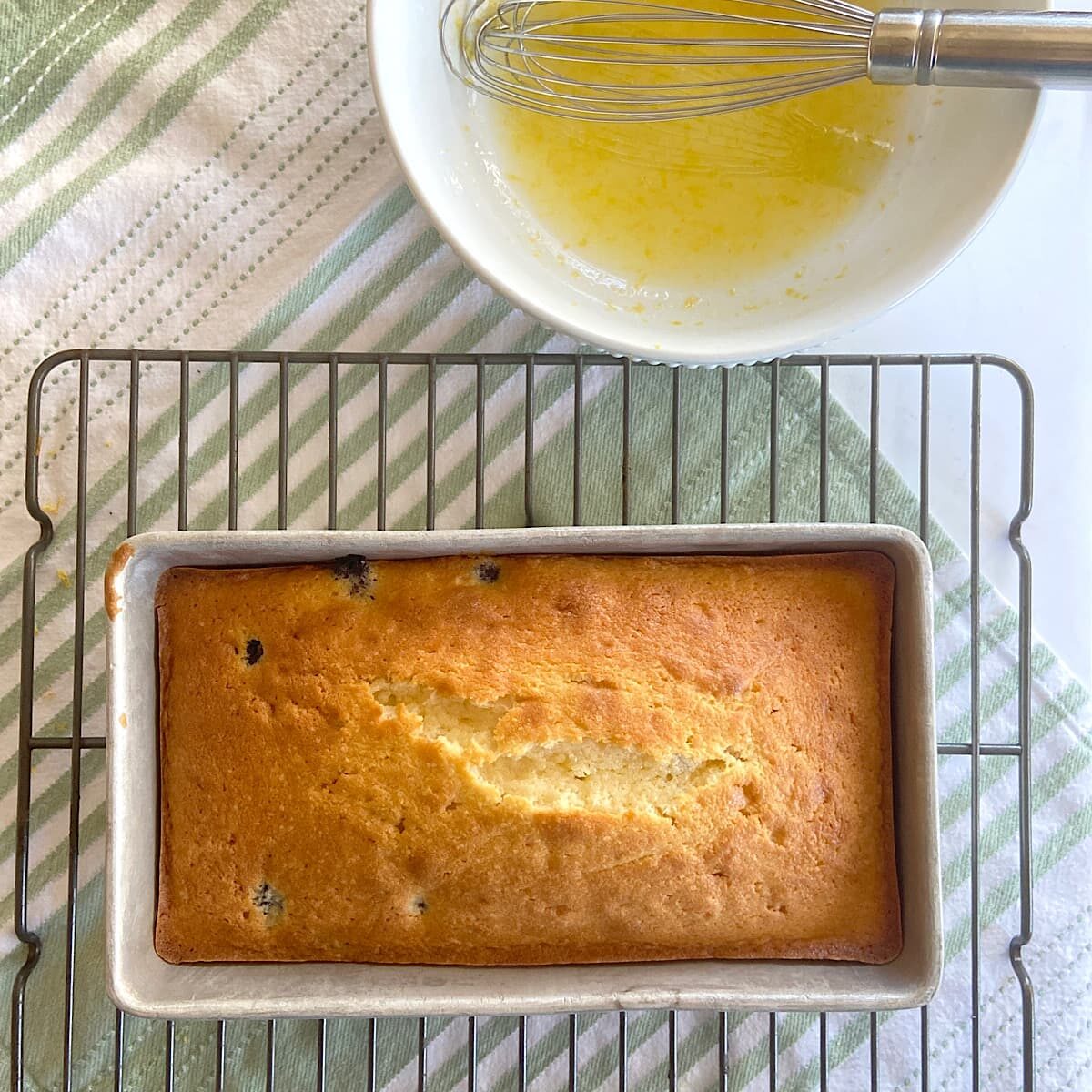 picture of loaf of lemon blueberry bread on rack with bowl of glaze