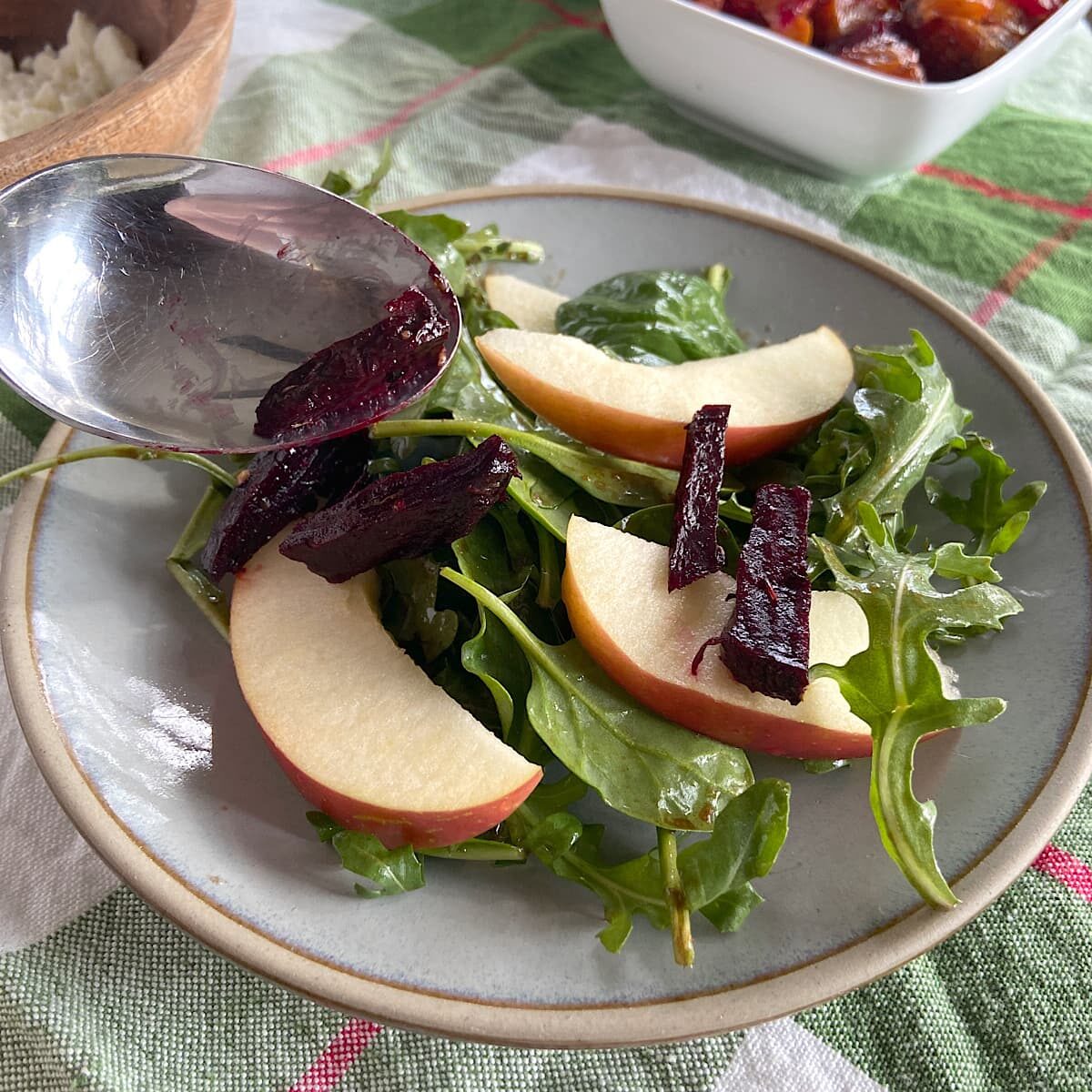 Layering beets over sliced apples, and greens on a plate.