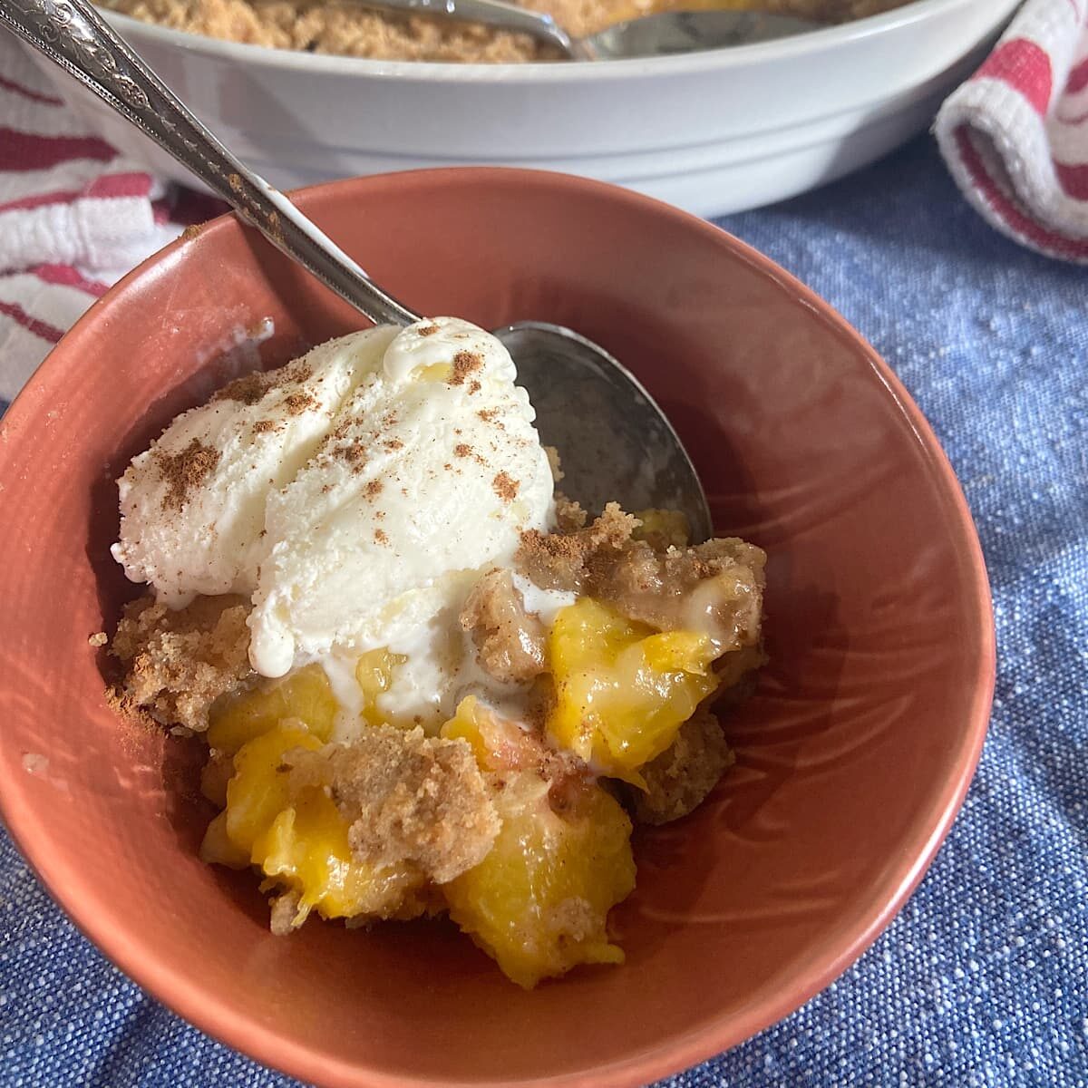 a serving of peach crisp with a scoop of ice-cream and a sprinkle of cinnamon