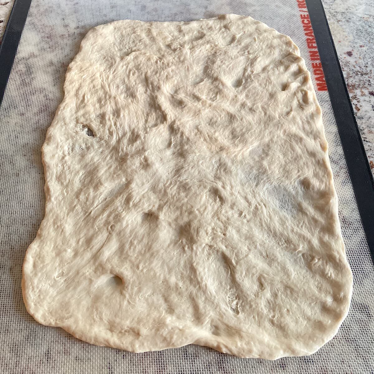 Thin Crust Pizza Dough rolled out on a silicon mat.