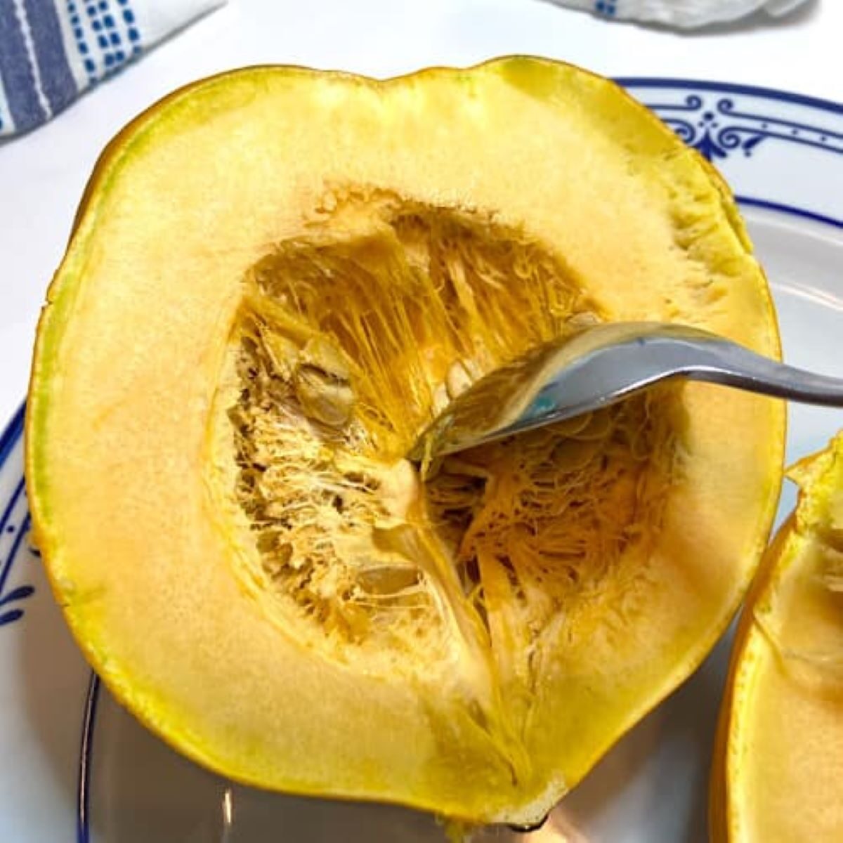 picture of half slice of acorn squash and using a spoon to remove seeds.