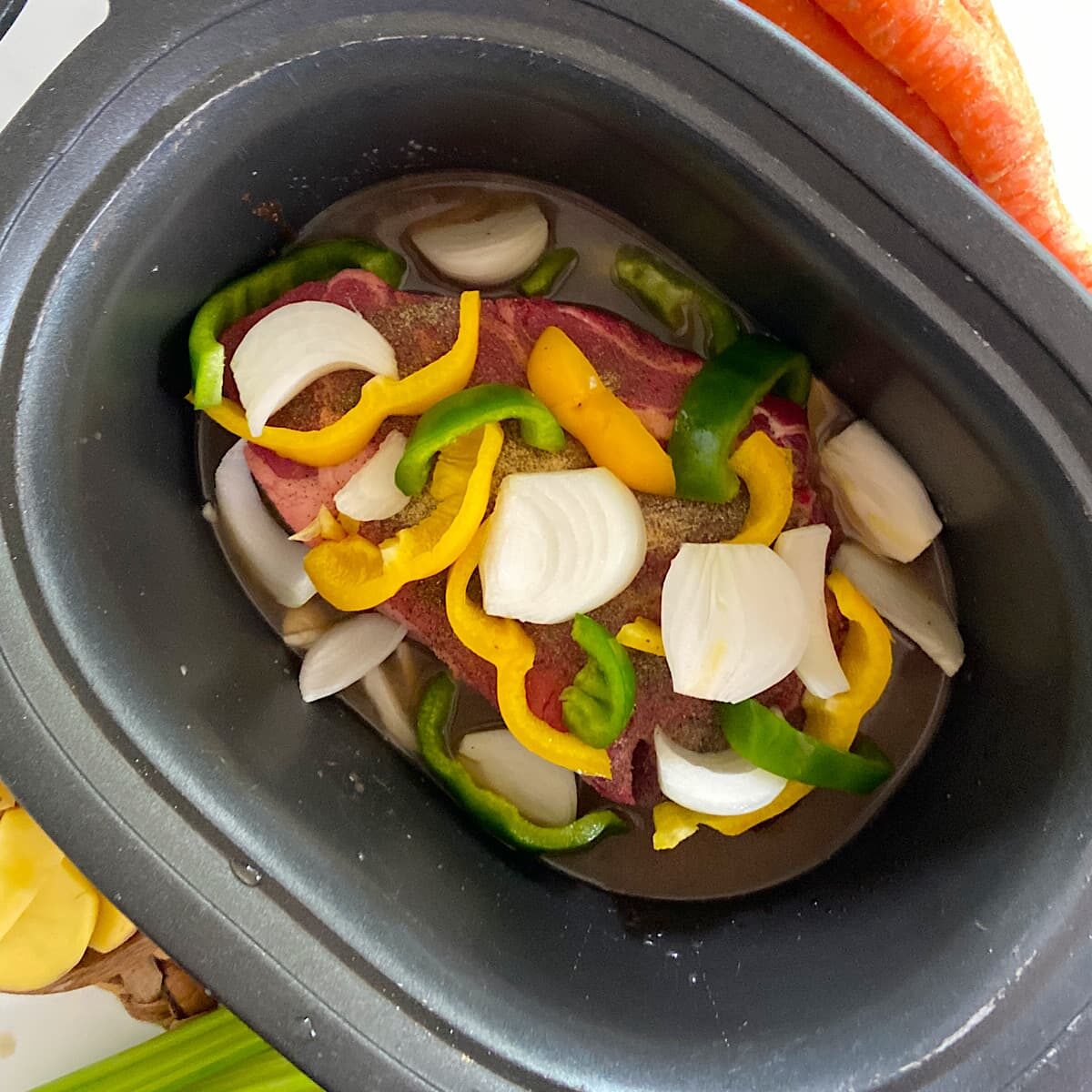 picture of slow cooker with pot roast, bell peppers, onion and broth.